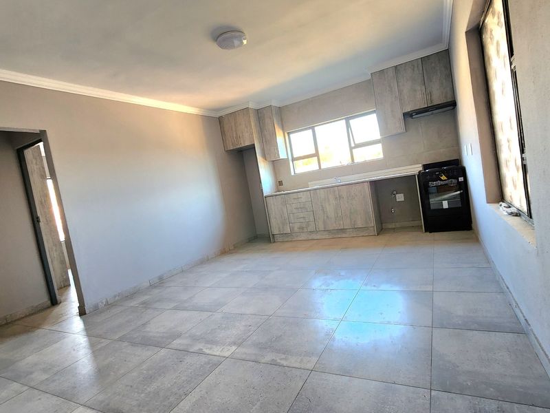 An open-plan living and kitchen area featuring modern tiled flooring, neutral walls, and built-in cabinetry with an integrated stove and extractor fan.