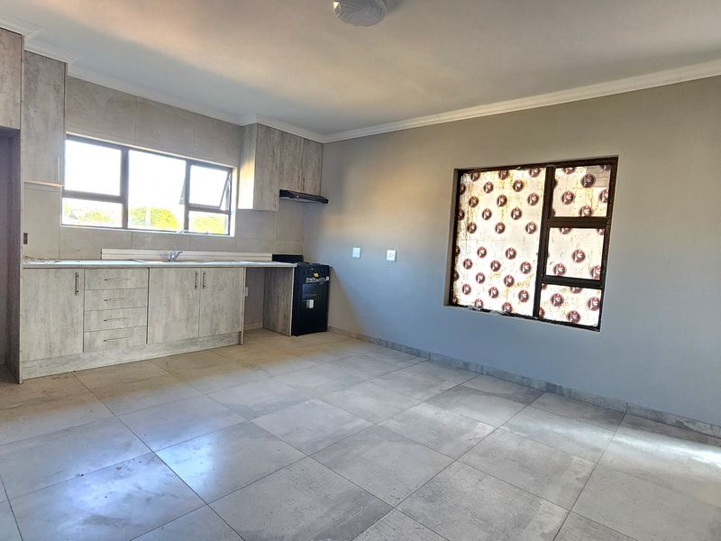 Open-plan living area featuring modern light-wood cabinetry, tiled flooring, and large windows providing ample natural light.