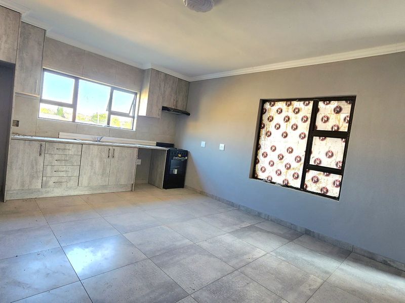 Open plan kitchen and living area featuring modern grey cabinetry, tiled flooring, and ample natural light through aluminium windows.