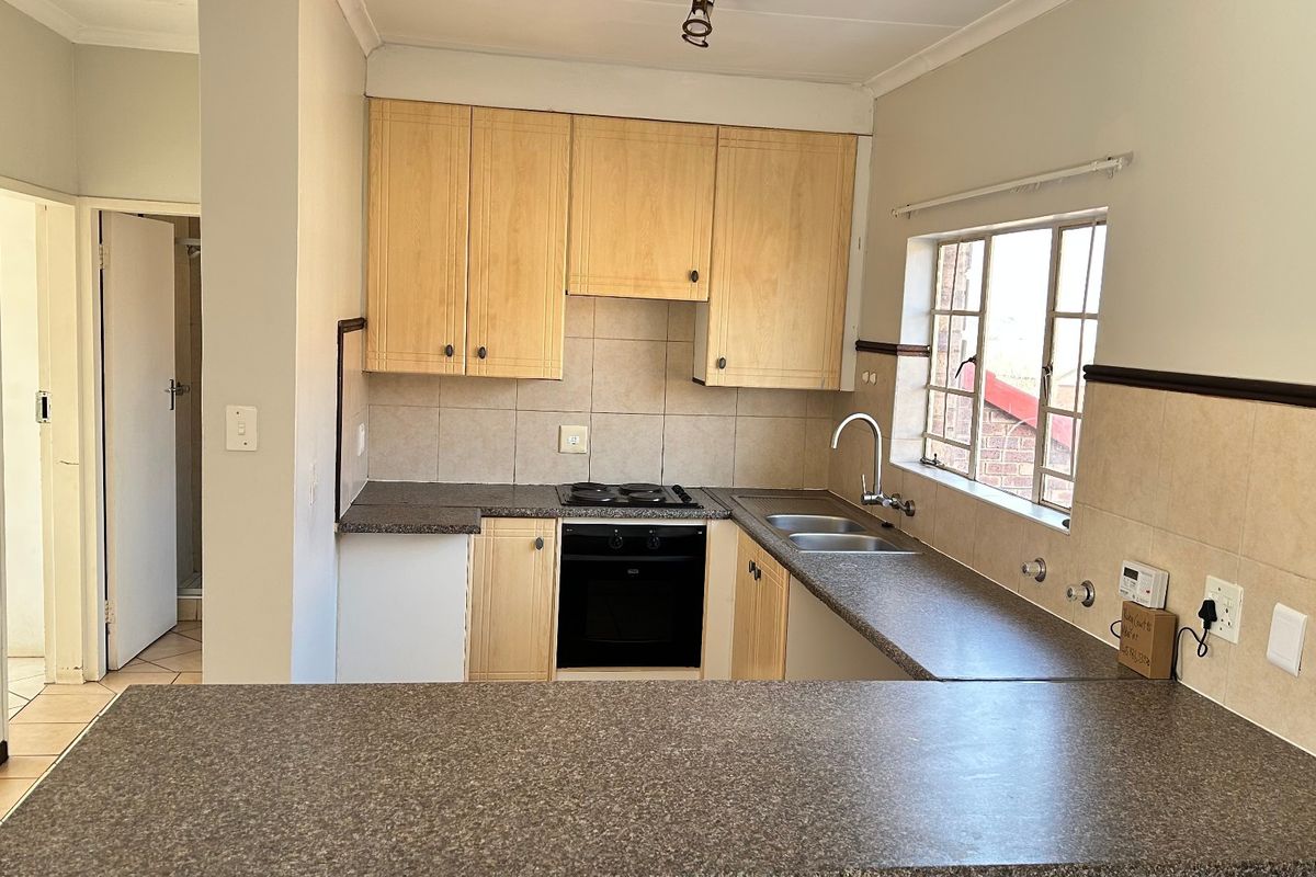A functional kitchen featuring light wood cabinetry, laminate countertops, a built-in oven and hob, and a convenient breakfast bar overlooking the space.