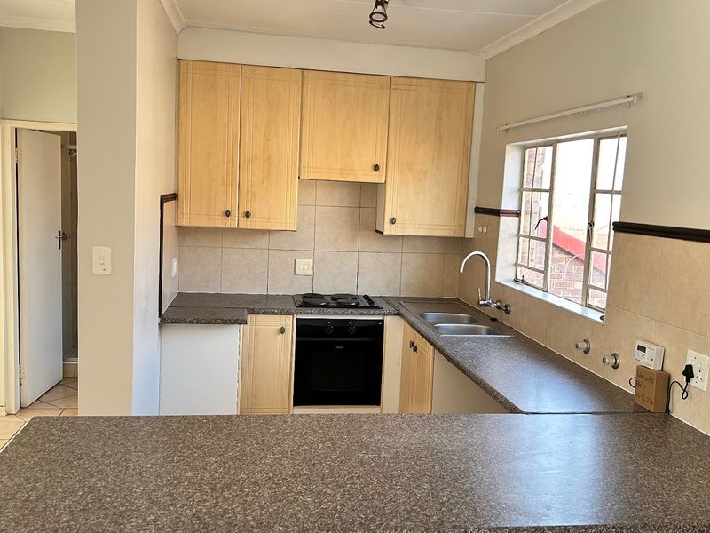 A functional kitchen featuring light wood cabinetry, laminate countertops, a built-in oven and hob, and a convenient breakfast bar overlooking the space.