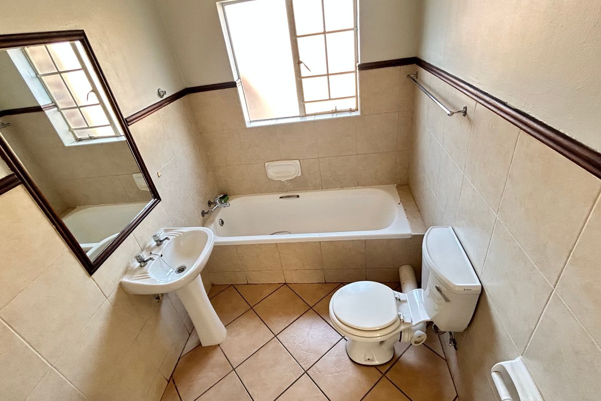 A functional bathroom featuring a pedestal basin, built-in bathtub, and toilet with neutral wall and floor tiling.