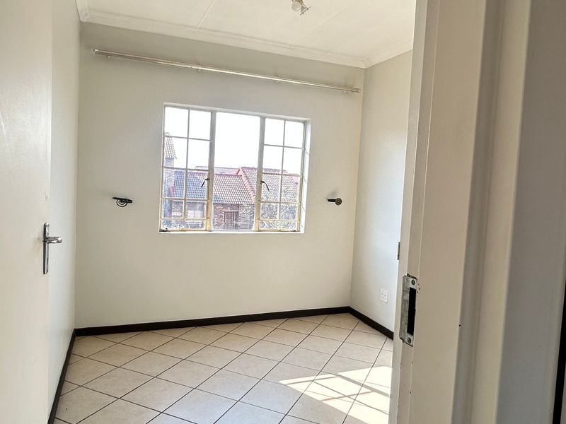 A bright, empty bedroom featuring neutral tiled flooring, white walls, and a window with muntins, providing a clean canvas for personalization.