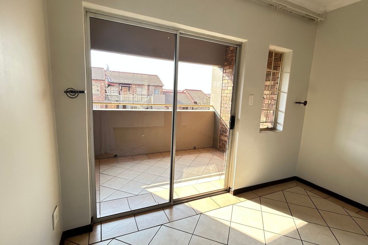 An empty bedroom featuring tiled flooring and a sliding glass door that opens onto a private balcony.