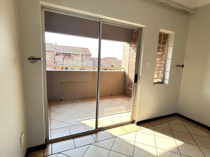 An empty bedroom featuring tiled flooring and a sliding glass door that opens onto a private balcony.