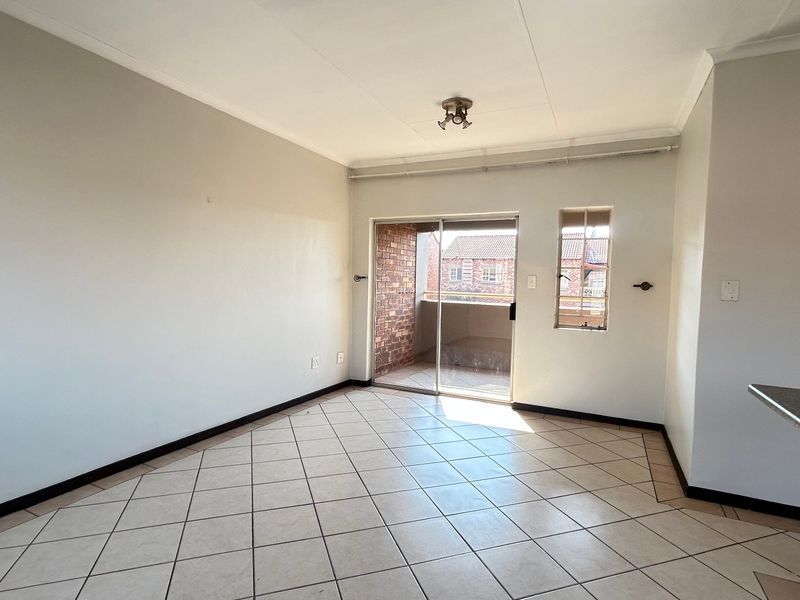An empty open-plan living area featuring tiled flooring, a sliding door leading to a balcony, and neutral wall finishes.