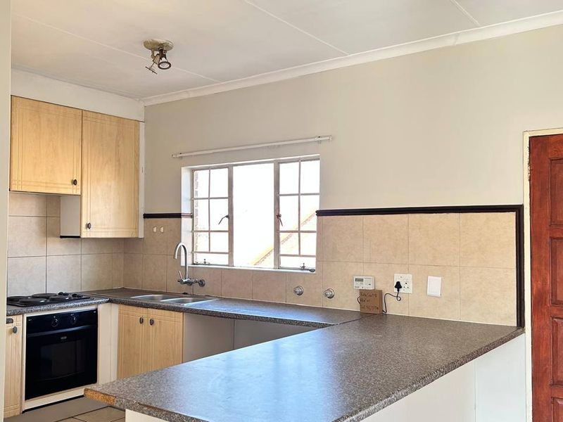 A functional kitchen featuring light wood cabinetry, laminate countertops, a built-in oven and hob, and a tiled backsplash.