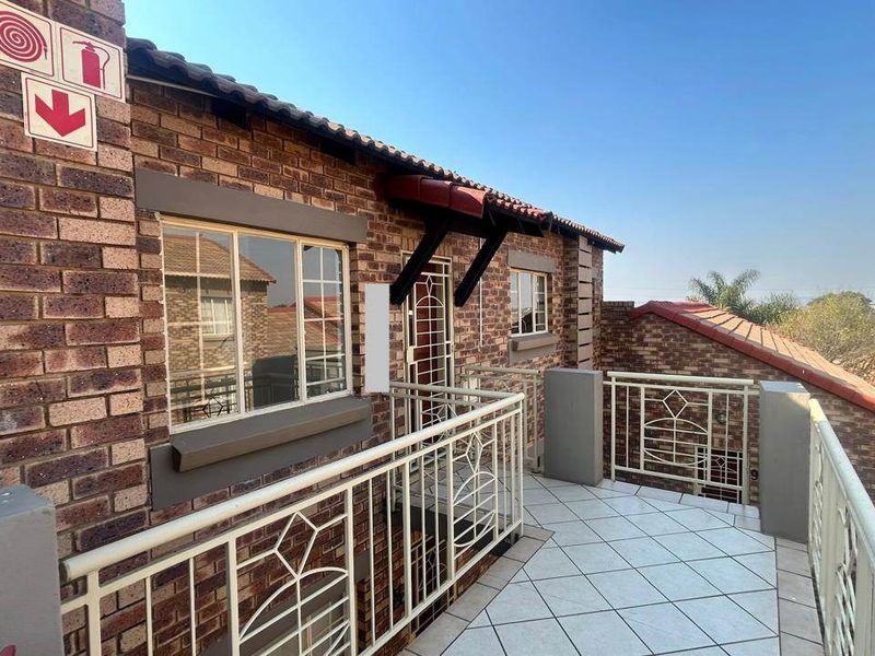 A spacious balcony featuring tiled flooring, a secure metal balustrade, and a classic brick exterior finish, offering a clear view of the surrounding complex.