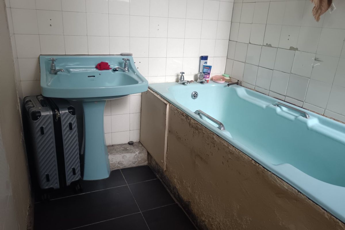 A dated bathroom featuring a vintage blue pedestal basin and bathtub, requiring significant renovation and tile repairs to modernize the space.