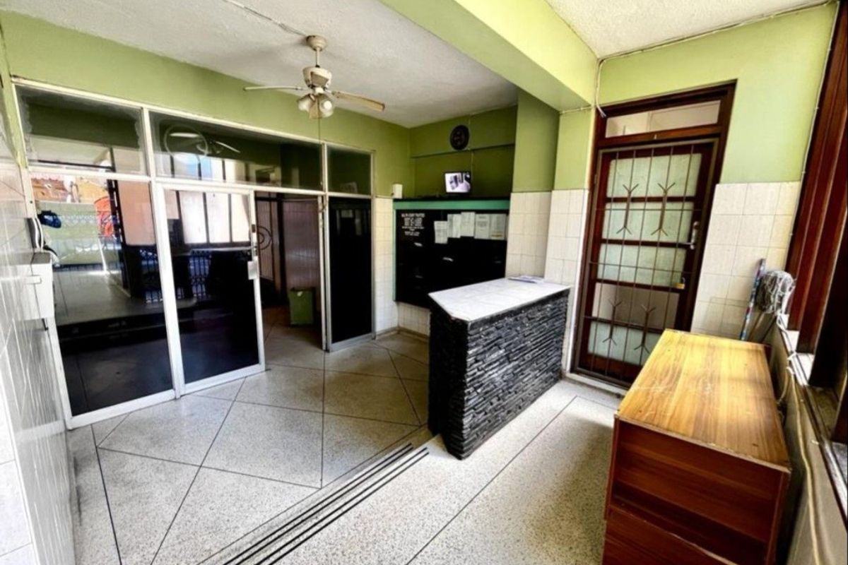Apartment building entrance lobby featuring a reception desk, tiled flooring, and security access points, requiring cosmetic updates to improve the overall aesthetic.