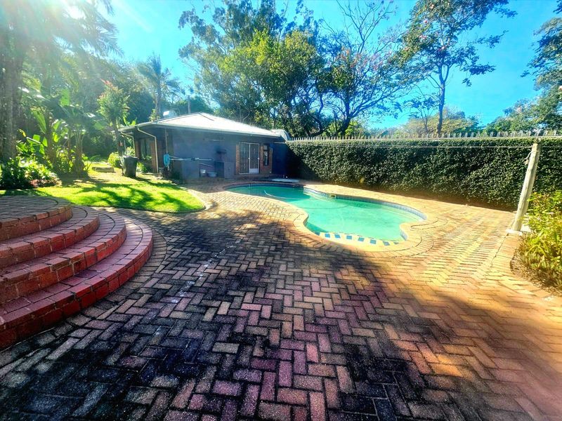 Outdoor pool area featuring a swimming pool, brick paved patio, and landscaped garden surroundings with perimeter hedging.