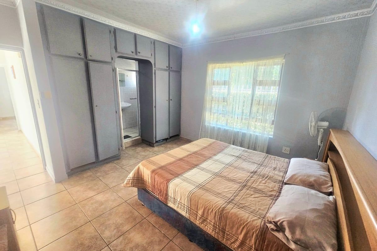 A bedroom featuring built-in cupboards, tiled flooring, and an en-suite bathroom entrance, offering a functional layout with potential for cosmetic updates.