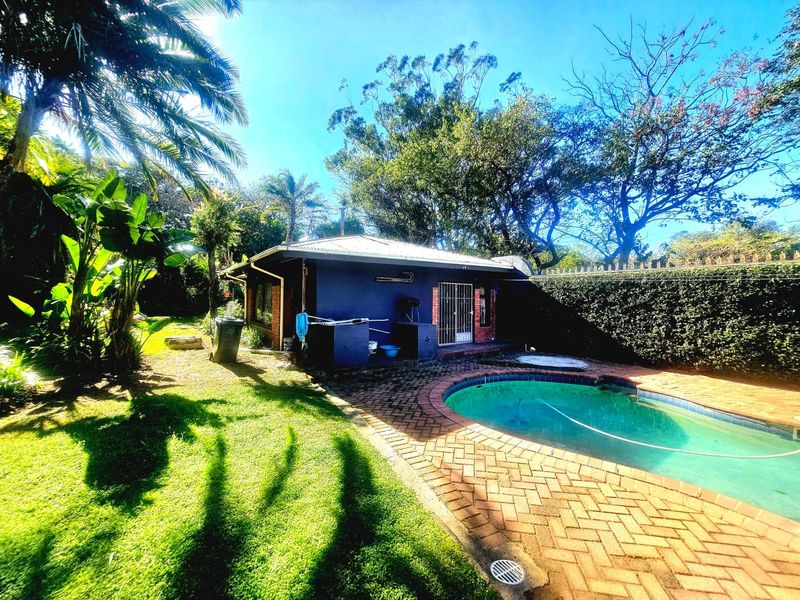 Rear exterior view featuring a swimming pool, brick paved patio area, and established garden surroundings.