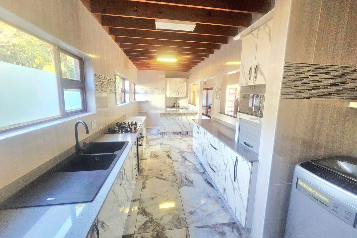 Modern kitchen featuring marble-look tiled floors, exposed timber beam ceiling, stone countertops, and integrated appliances with ample cabinetry and a double basin sink.