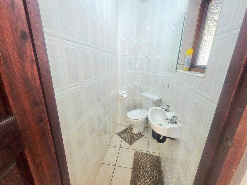 A compact, fully tiled bathroom featuring a wall-mounted basin and a standard toilet, with an obscured glass window for privacy.