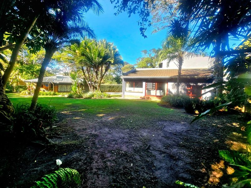 A spacious, lush garden featuring mature trees and a view of the rear building facade with tiled roofing.