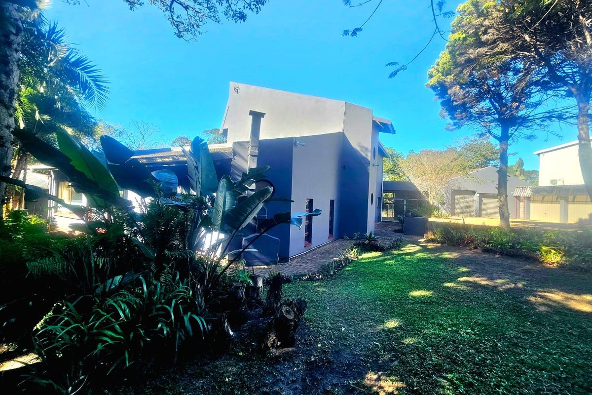 A view of the rear exterior of the property, featuring a well-maintained garden, mature trees, and a paved walkway leading along the building.