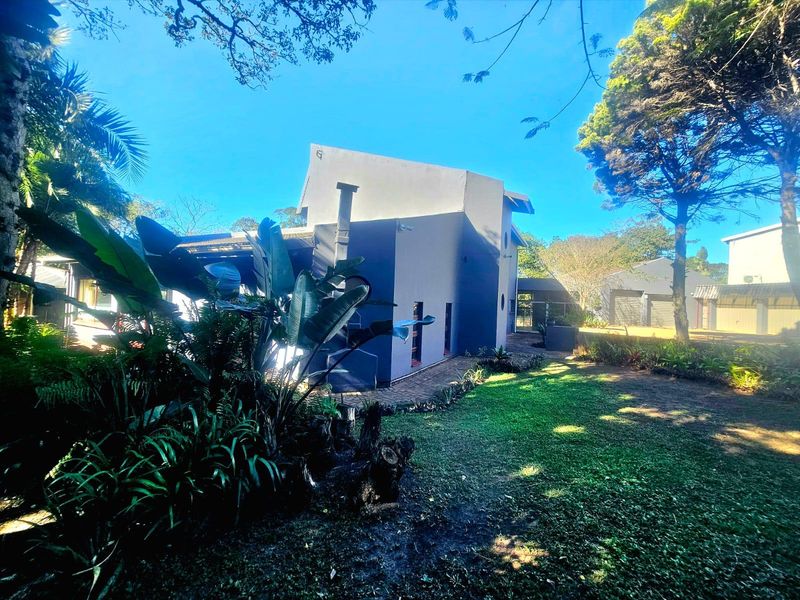 A view of the rear exterior of the property, featuring a well-maintained garden, mature trees, and a paved walkway leading along the building.
