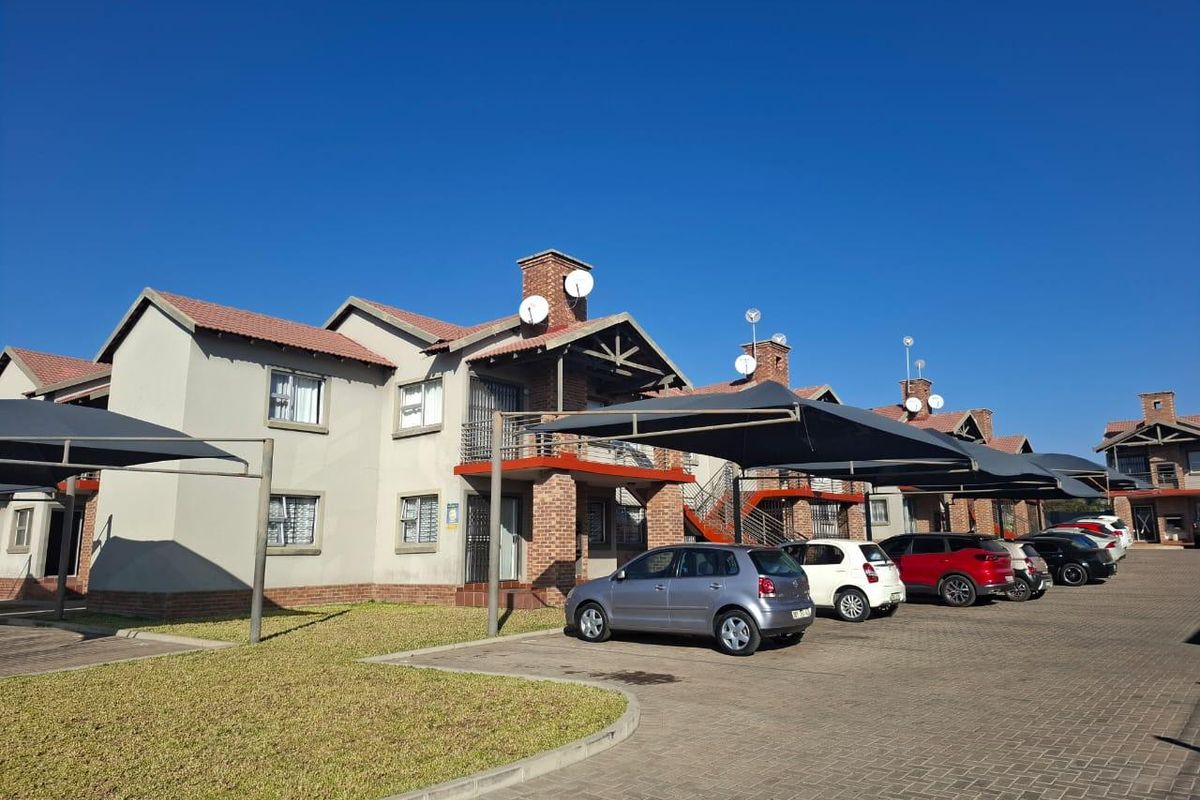 Exterior view of a townhouse complex featuring brick and plaster facades, tiled roofs, and covered parking bays with paved driveway access.