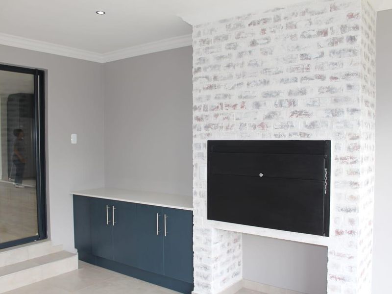 Modern living area featuring a striking white-washed exposed brick fireplace, sleek built-in cabinetry with stone countertop, and large sliding glass doors.