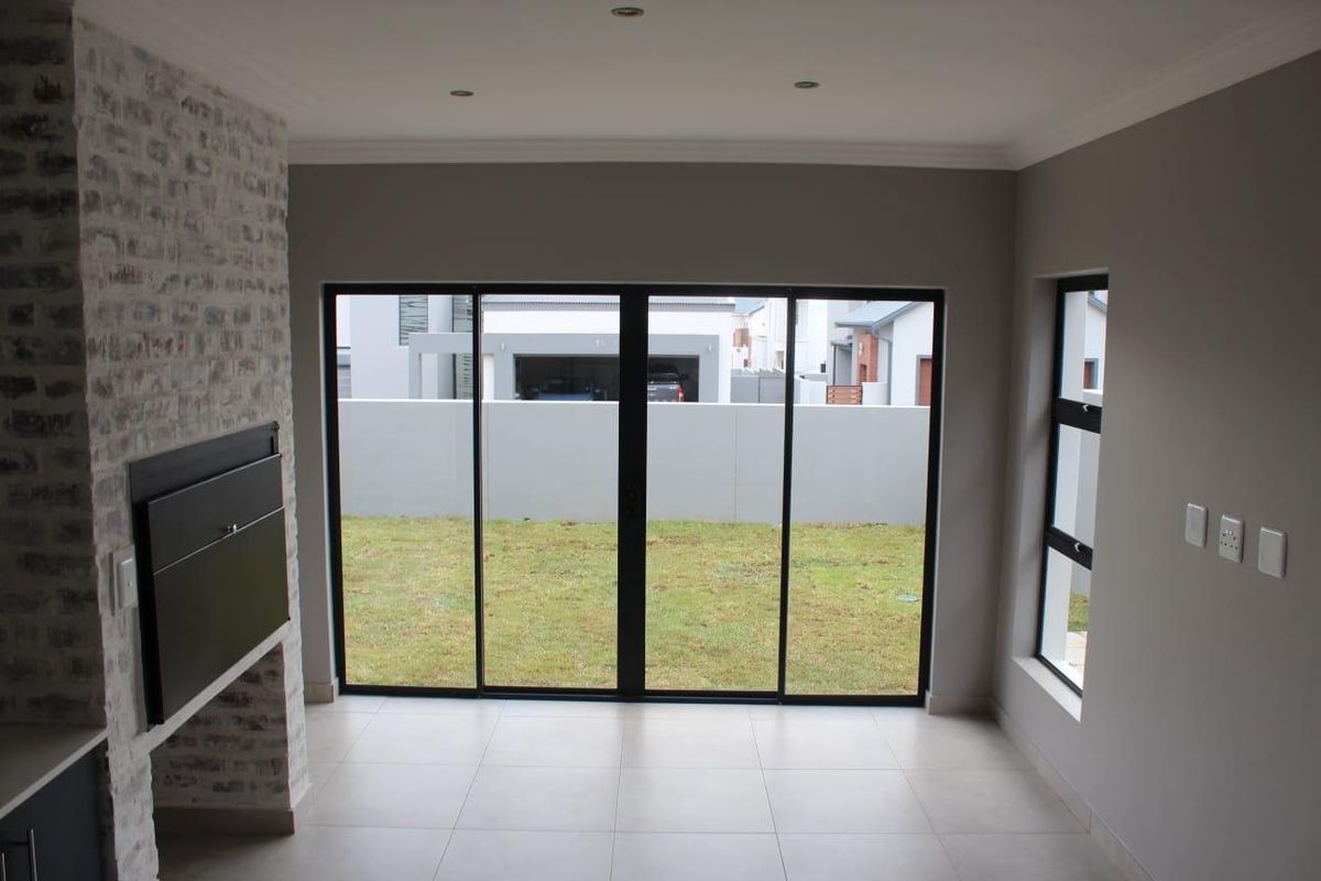 A bright, empty living room featuring a modern built-in fireplace with an exposed brick finish, tiled floors, and large sliding doors opening to the garden.