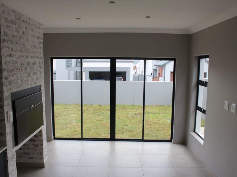 A bright, empty living room featuring a modern built-in fireplace with an exposed brick finish, tiled floors, and large sliding doors opening to the garden.