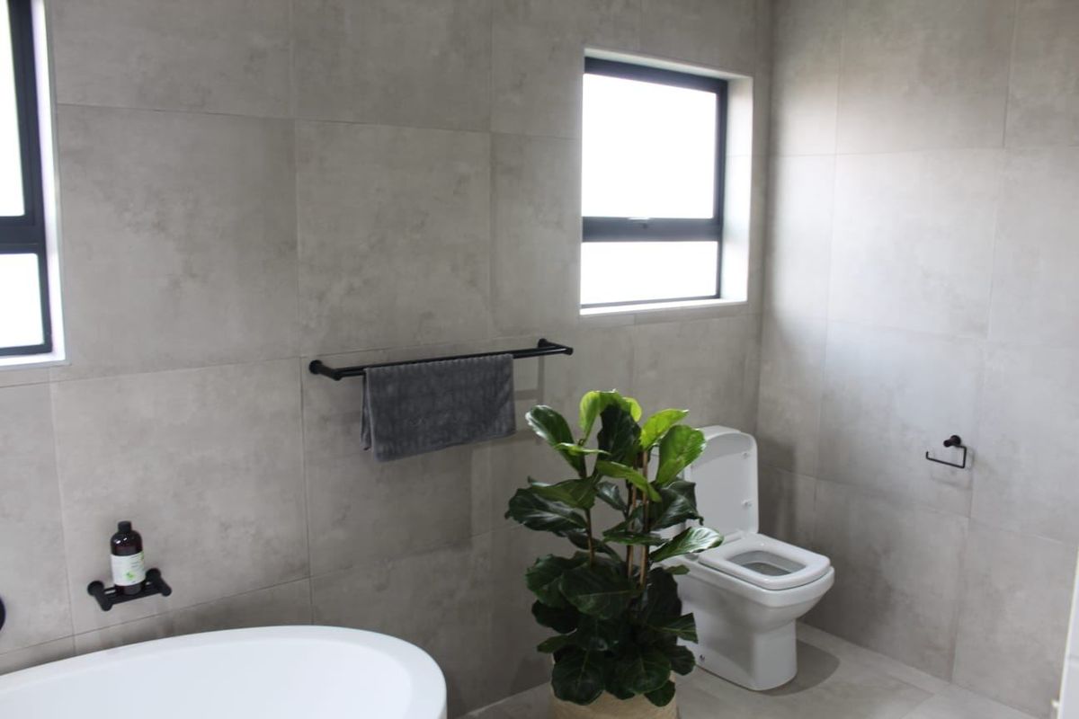 Modern bathroom featuring large format grey wall and floor tiles, a freestanding bathtub, and contemporary black fixtures.
