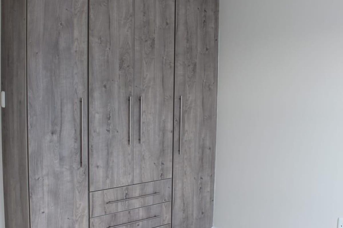 A clean bedroom featuring modern grey wood-grain built-in wardrobes, light laminate flooring, and neutral wall finishes.