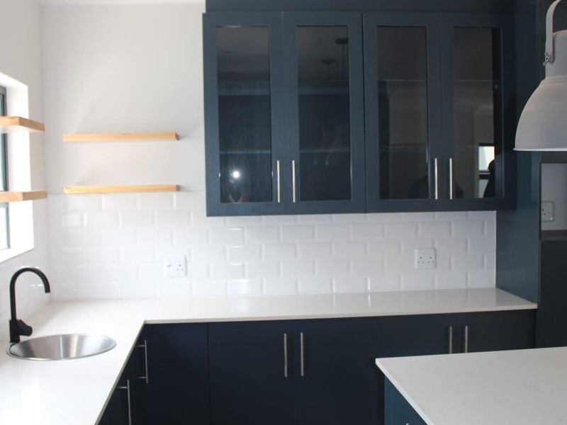Modern kitchen featuring dark blue cabinetry, white quartz countertops, subway tile backsplash, and a functional island, offering a clean and contemporary aesthetic.