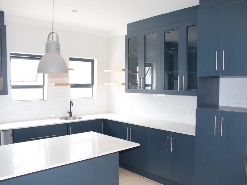 Modern kitchen featuring navy blue cabinetry, white quartz countertops, subway tile backsplash, and a central island with pendant lighting.