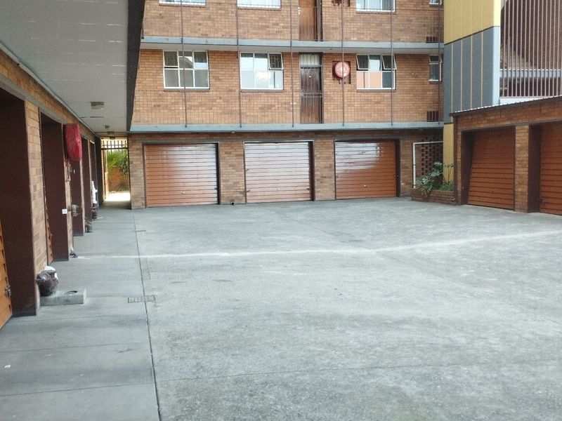 A view of a residential apartment complex courtyard featuring multiple individual lock-up garages with roll-up doors and a concrete driveway.