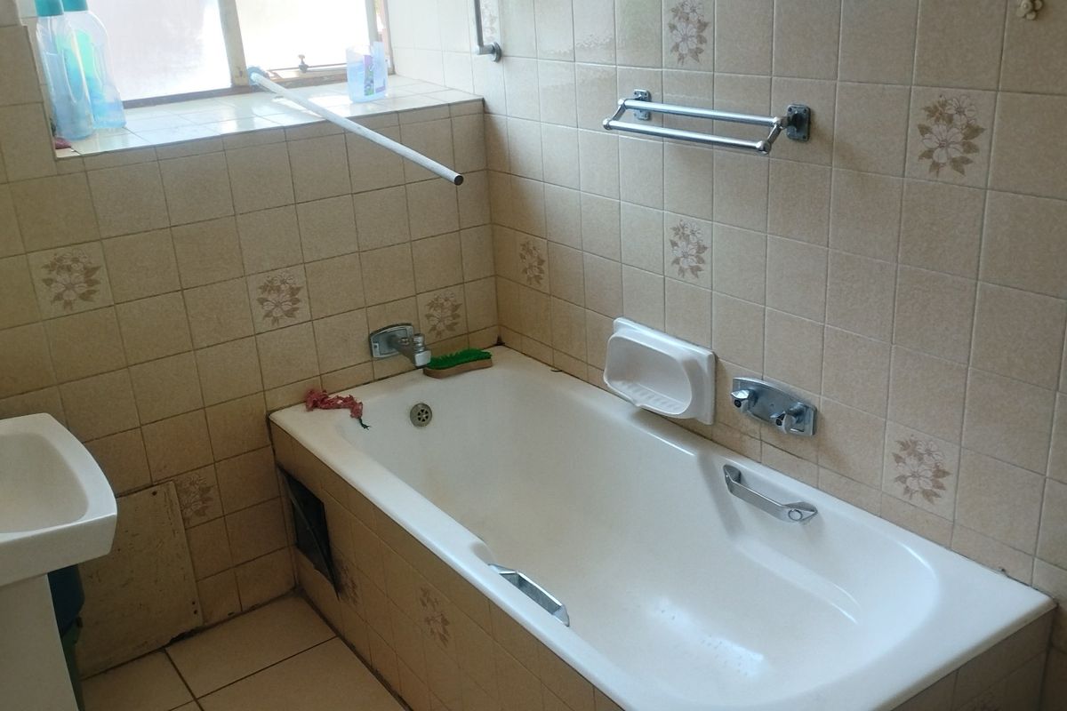 A dated bathroom featuring a standard bathtub, pedestal basin, and full-height wall tiling, offering potential for a modern renovation.