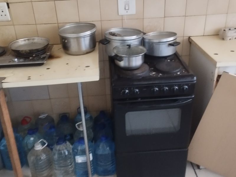 A dated kitchen area featuring a freestanding electric stove, hob, and tiled backsplash, currently showing signs of wear and missing cabinetry components.
