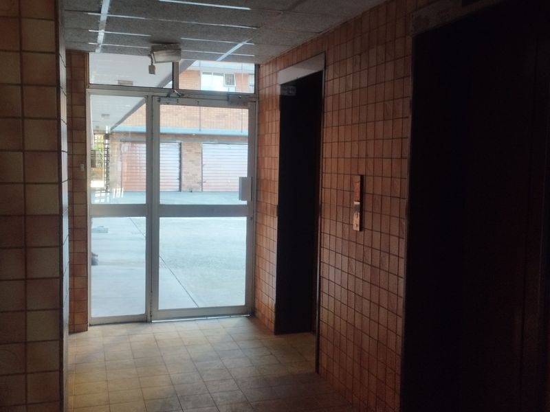 A dated apartment building entrance lobby featuring tiled walls, tiled flooring, and elevator access.