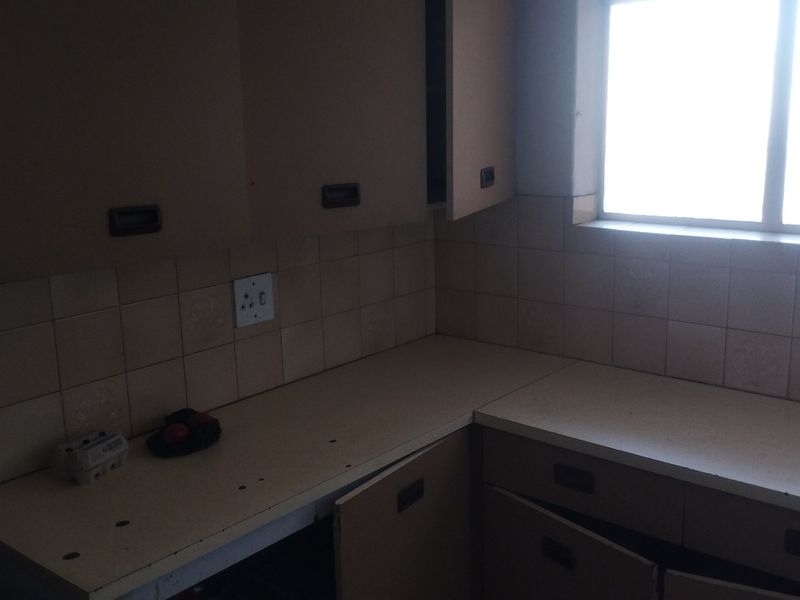 A dated kitchen area featuring original cabinetry, tiled backsplash, and laminate countertops, requiring modernization to improve functionality and aesthetic appeal.