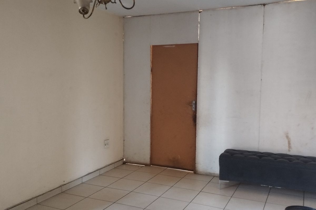 A living area featuring tiled flooring and a simple internal door, currently showing signs of wear on the wall panels and door surface.