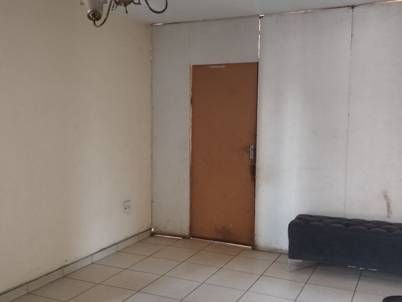 A living area featuring tiled flooring and a simple internal door, currently showing signs of wear on the wall panels and door surface.