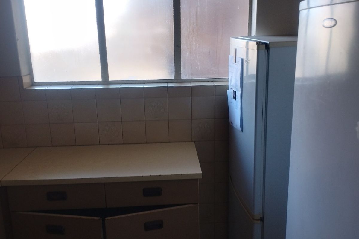 A dated kitchen area featuring tiled splashbacks, laminate countertops, and built-in cabinetry in need of repair or modernization.