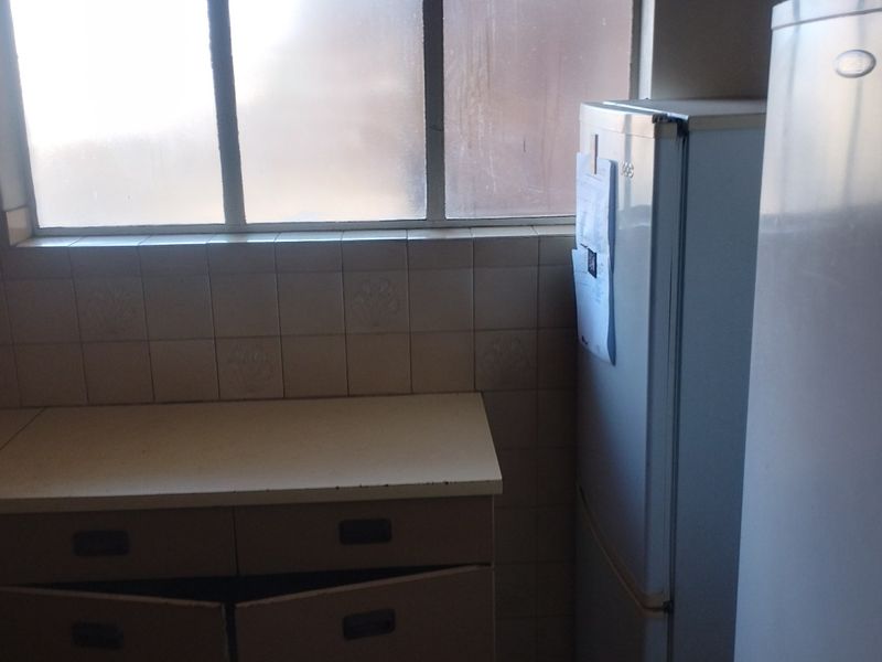 A dated kitchen area featuring tiled splashbacks, laminate countertops, and built-in cabinetry in need of repair or modernization.