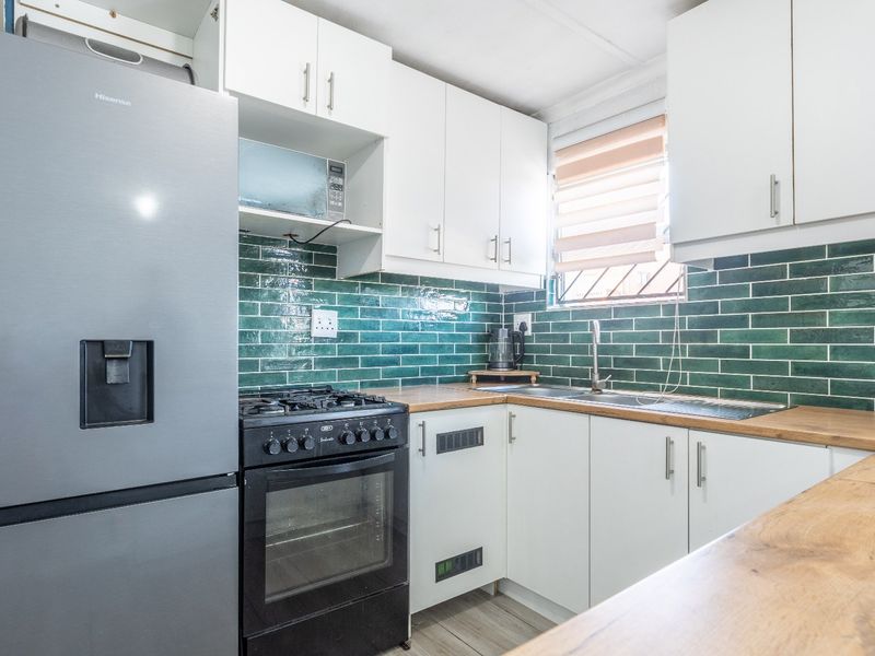 A functional kitchen featuring white cabinetry, wooden countertops, a green subway tile backsplash, and a built-in gas stove with oven.