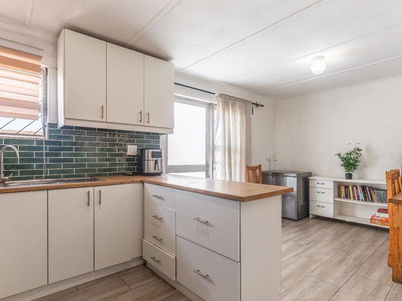 Open-plan kitchen and dining area featuring white cabinetry, wooden countertops, green subway tile backsplash, and durable laminate flooring.