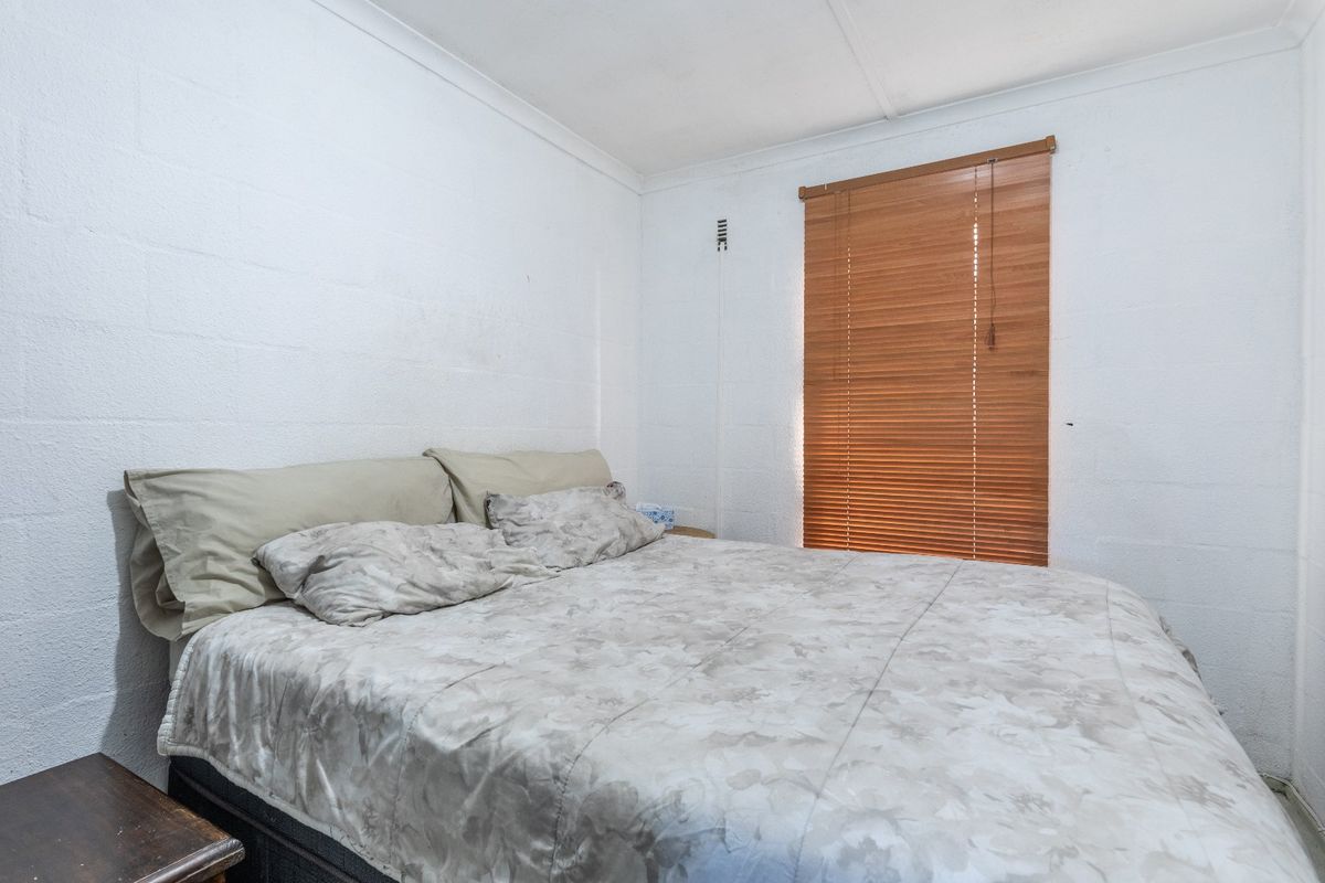 A functional bedroom featuring white painted blockwork walls and timber venetian blinds, providing a neutral base for potential interior updates.