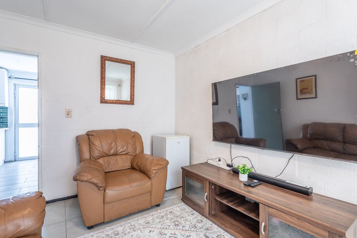 A living room featuring tiled flooring and exposed blockwork walls, with an open transition to the adjacent kitchen area.