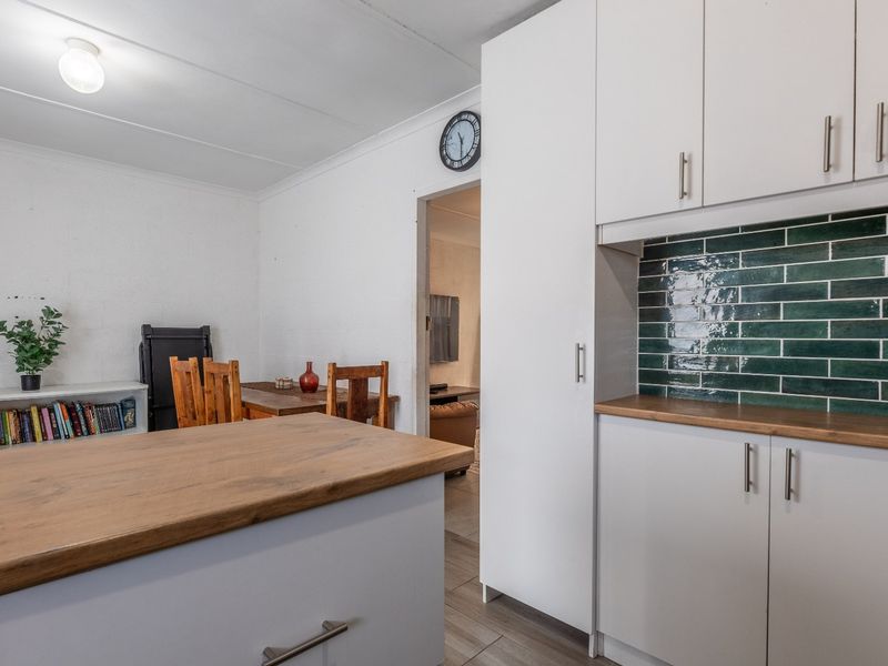 A functional kitchen area featuring modern white cabinetry, timber-look countertops, and a stylish green subway tile backsplash, seamlessly connected to the adjacent living space.