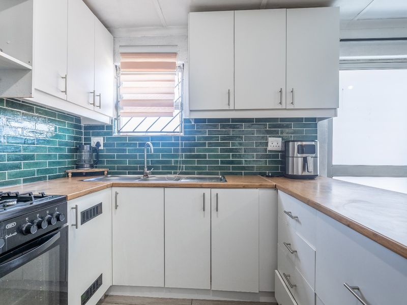 A functional kitchen featuring white cabinetry, wooden countertops, a gas stove with oven, and a striking green tiled backsplash.