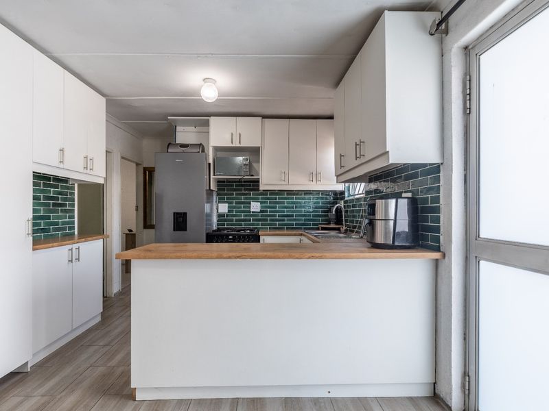 A functional kitchen featuring white cabinetry, green subway tile backsplash, wooden countertops, and direct access to the exterior via a glass panel door.