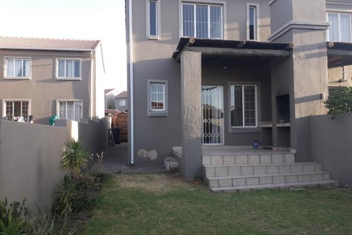 Rear view of the property featuring a covered patio with a built-in braai, security gates, and a small private garden area.