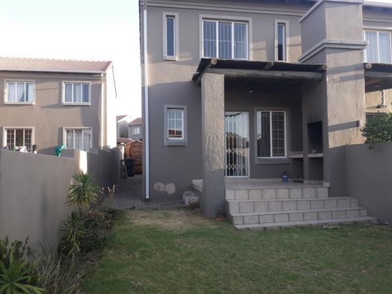 Rear view of the property featuring a covered patio with a built-in braai, security gates, and a small private garden area.