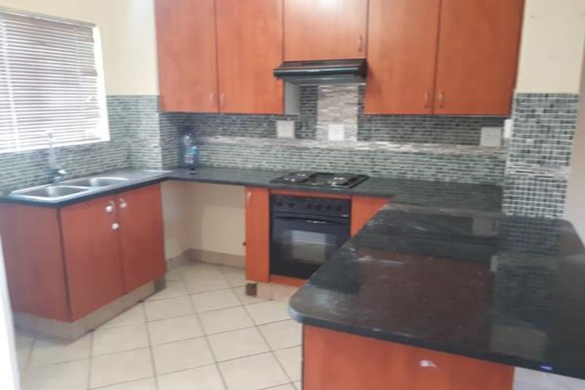 A functional kitchen featuring wooden cabinetry, granite countertops, a mosaic tile backsplash, and built-in cooking appliances with a breakfast bar area.