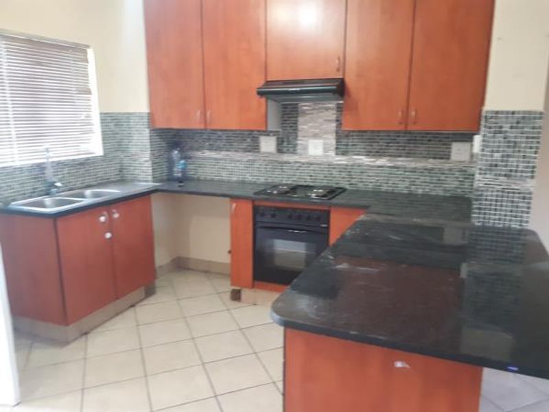 A functional kitchen featuring wooden cabinetry, granite countertops, a mosaic tile backsplash, and built-in cooking appliances with a breakfast bar area.